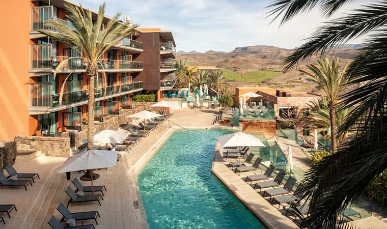 Das Salobre Hotel Resort ist ein moderner Rückzugsort mit einem großen Außenpool, der von Sonnenliegen und Palmen umgeben ist. Die mehrstöckigen Gebäude mit Balkonen bieten einen Blick auf die malerischen Hügel und den klaren Himmel im Hintergrund.