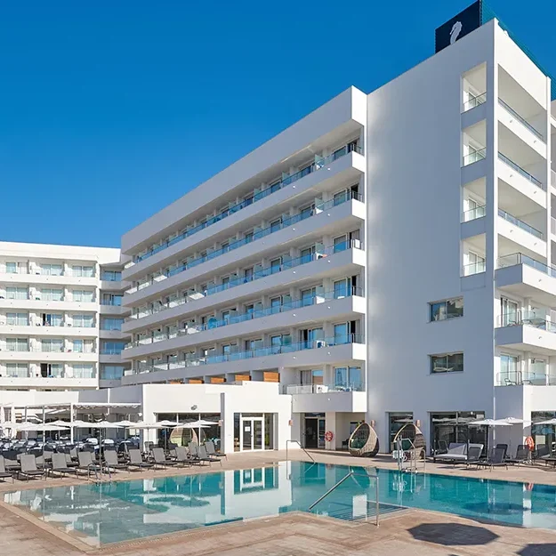 Das moderne, weiße Hotel „Hipotels Flamenco“ mit seinen zahlreichen Balkonen liegt direkt an einem klarblauen Swimmingpool, der von leeren Liegestühlen unter einem strahlend blauen Himmel umgeben ist.