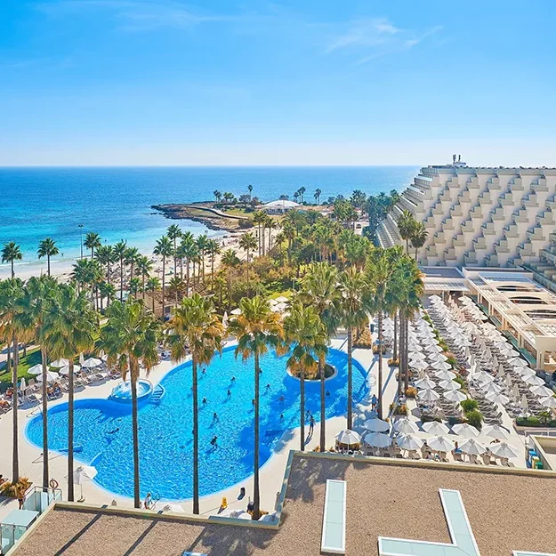 Das Hipotels Flamenco ist ein großes Resort direkt am Strand mit einem herzförmigen Pool, der von Palmen und Sonnenliegen umgeben ist und einen Blick auf den Sandstrand und das blaue Meer unter einem klaren Himmel bietet.