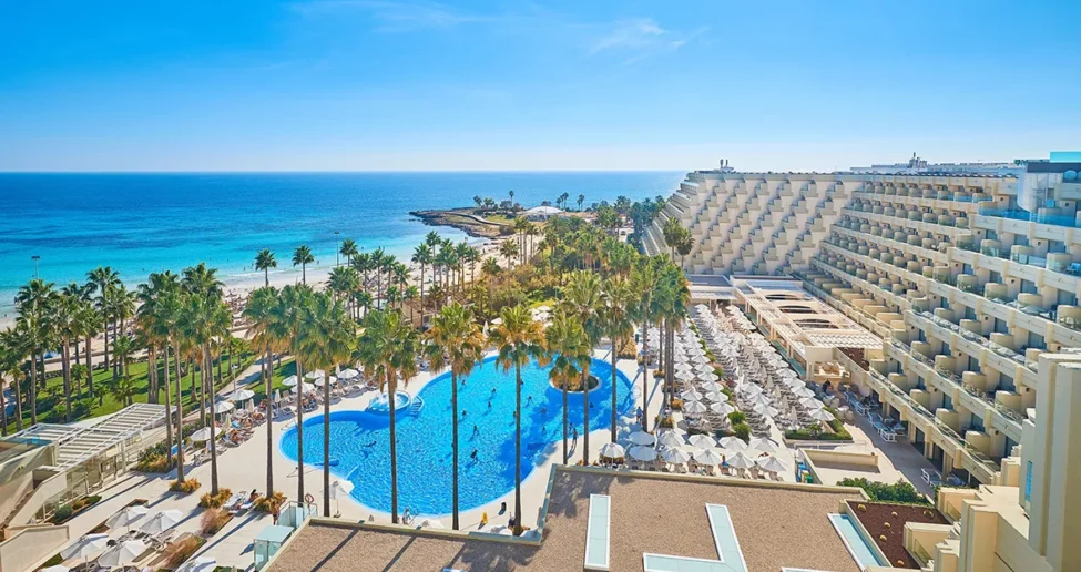 Das Hipotels Flamenco ist ein großes Resort direkt am Strand mit einem herzförmigen Pool, der von Palmen und Sonnenliegen umgeben ist und einen Blick auf den Sandstrand und das blaue Meer unter einem klaren Himmel bietet.