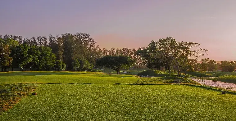 Ein Golfplatz mit sorgfältig gemähtem Rasen, umgeben von Bäumen unter einem klaren Himmel bei Sonnenuntergang. Schatten ziehen sich über das Grün und schaffen eine ruhige und friedliche Szenerie – eine idyllische Kulisse für eine Golf-Gruppenreise nach Südostasien, bei der Freunde gemeinsam in aller Ruhe das Spiel genießen können.