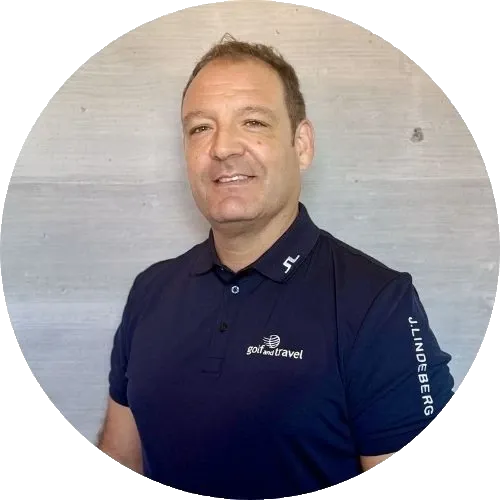 Ein Mann in einem marineblauen Golf- und Reise-Poloshirt steht vor einem hellgrauen Hintergrund und lächelt in die Kamera.