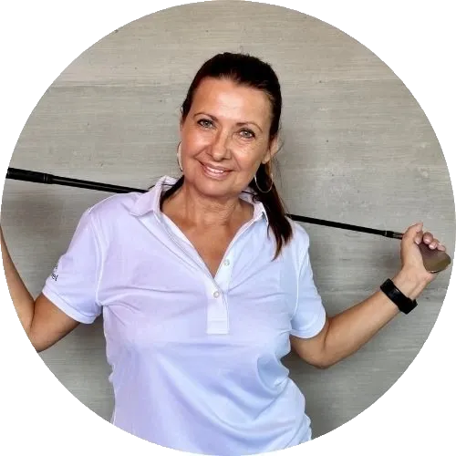 Eine Frau in einem weißen Polohemd lächelt, während sie einen Golfschläger über die Schultern trägt, und steht vor einem schlichten, hellen Hintergrund.