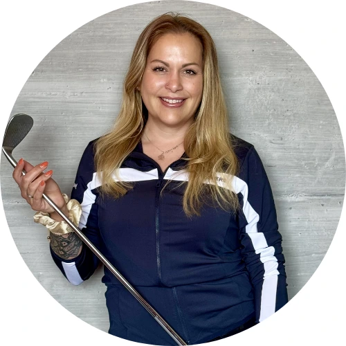Romina Nowak, mit langen blonden Haaren und einem strahlenden Lächeln, steht vor einer grauen Betonwand, trägt eine marineblaue und weiße Jacke und hält einen Golfschläger in der rechten Hand.