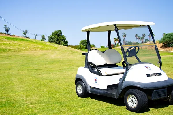 Ein weißer Golfwagen, der auf einem grünen Golfplatz unter strahlend blauem Himmel geparkt ist, mit Bäumen und grasbewachsenen Hügeln im Hintergrund – Szenen wie diese sind auf den atemberaubenden Golfplätzen Portugals an der Tagesordnung.