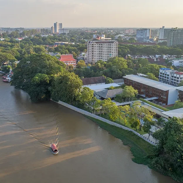 Luftaufnahme eines Flusses, der sich durch eine Stadt schlängelt, mit üppig grünen Bäumen an den Ufern, modernen Gebäuden in der Nähe und einem kleinen Boot, das unter einem teilweise bewölkten Himmel auf dem Wasser dahingleitet.