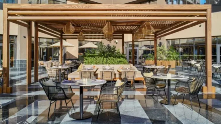 Sitzbereich im Freien mit schwarzen Korbstühlen, runden Tischen und einer Holzpergola. An der Pergola hängen Pendelleuchten, und der Bereich ist von Grünpflanzen umgeben – ein einladender Ort zum Entspannen nach einer Golfrundreise durch Irland.