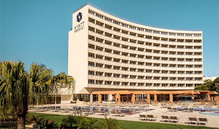 Das MiM Sotogrande Meliá ist ein großes, modernes Hotelgebäude mit geschwungenem Design und zahlreichen Balkonen. Es ist umgeben von Palmen, Sitzgelegenheiten im Freien und einem Swimmingpool unter strahlend blauem Himmel.