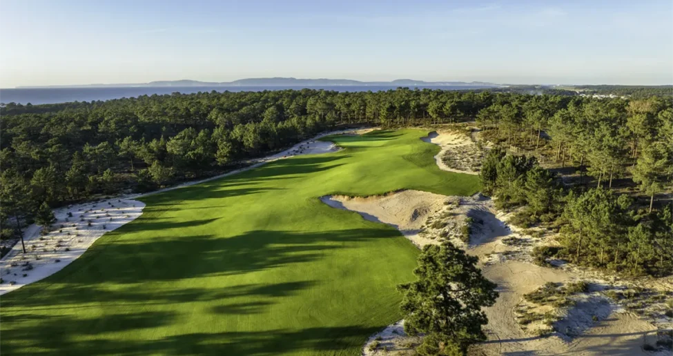 Luftaufnahme eines üppig grünen Golfplatzes, umgeben von dichtem Wald und Sandbunkern, vor dem Hintergrund ferner Berge und eines blauen Himmels – perfekt für eine Irland-Rundreise entlang der Ostküste.