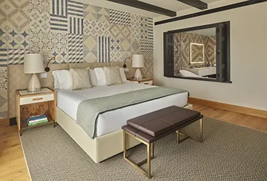 Deluxe King Room Viceroy at Ombria Algarve Ein modernes Schlafzimmer im „Viceroy at Ombria Algarve“ verfügt über eine gemusterte Akzentwand, ein großes Bett mit weißer Bettwäsche und einer grünen Tagesdecke, zwei Nachttische mit Lampen, eine Bank am Fußende des Bettes sowie einen großen Spiegel an der Wand.